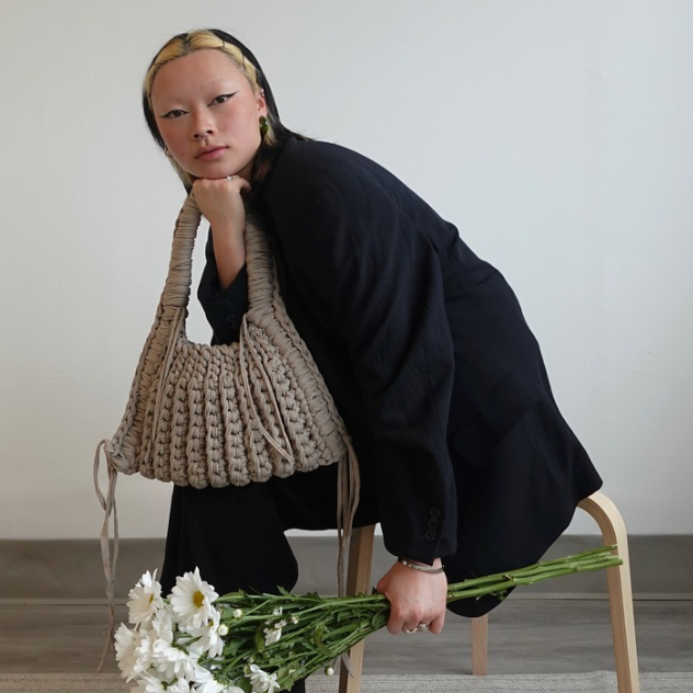 Person holding a woven bag and flowers in a minimalistic setting