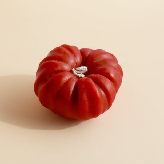 A red heirloom tomato candle on a cream background