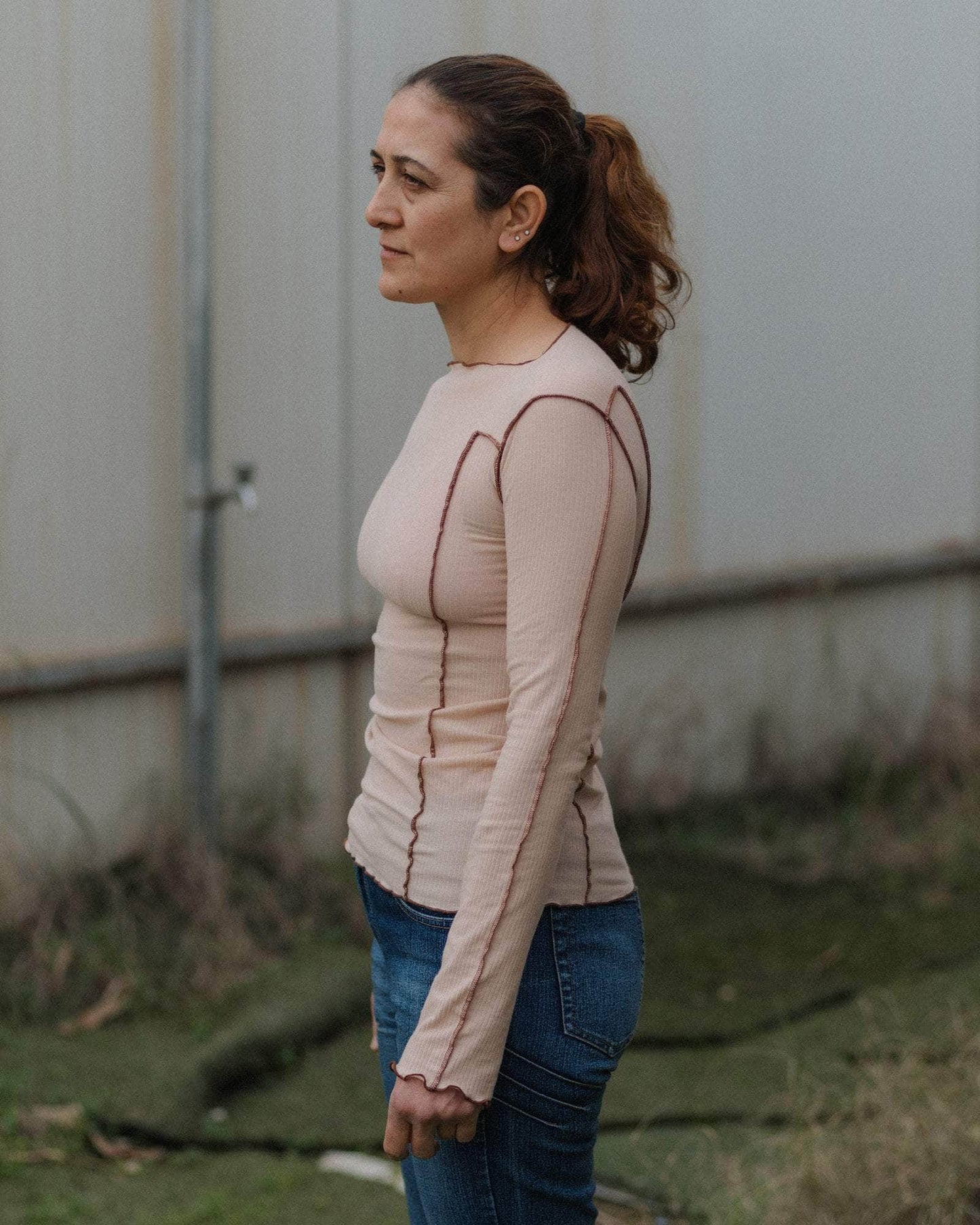 Woman wearing a beige long-sleeve shirt with brown stitching against a plain background