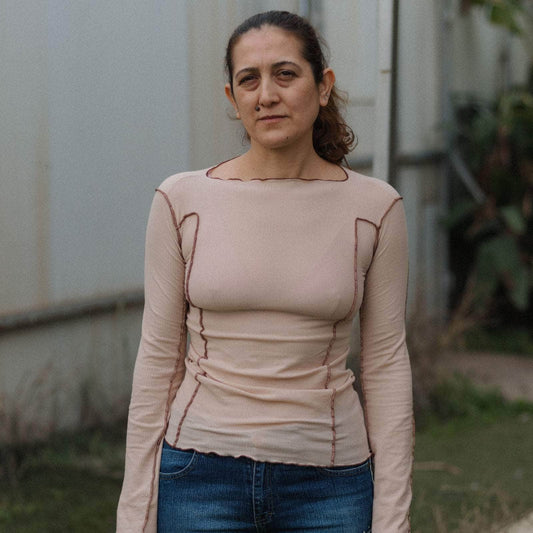 Woman wearing a beige long-sleeve top with visible seams, standing outdoors.