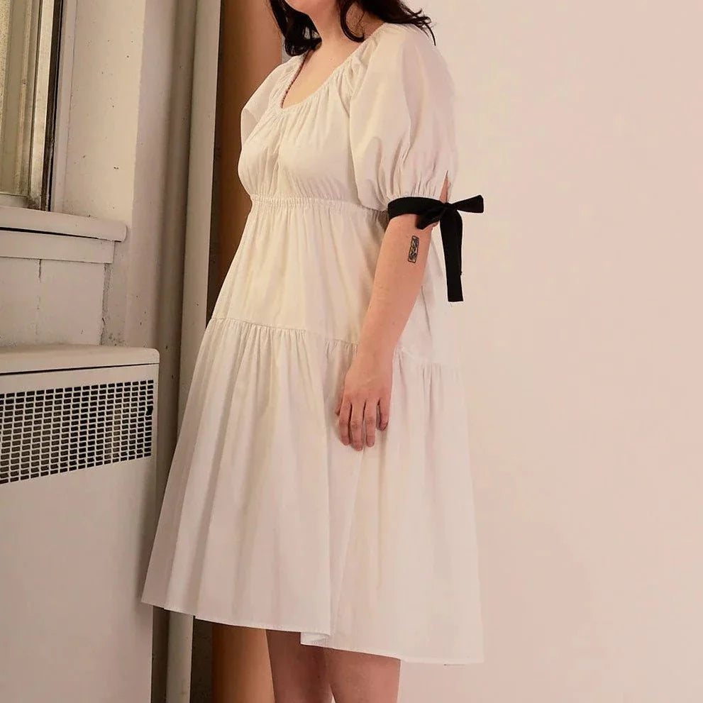 Overall white dress with extra puffy sleeves, gathered tiers, and black bow-tie details, the Jolen dress is both elegant and incredibly comfortable too. It's fully lined with cotton, slips on easily over head, and has pockets.