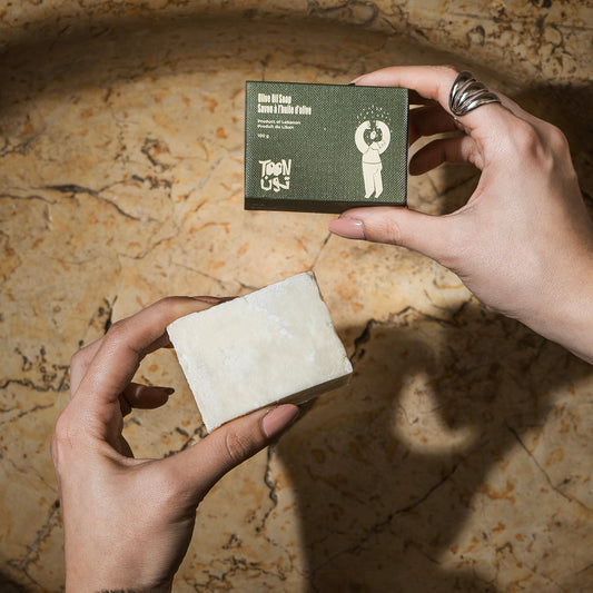 Person holding a bar of soap and its packaging on a textured surface