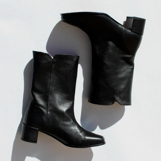 About Arianne black leather pull on boot with almond shaped toe, block heel, and v- shaped dip detail at top of shaft 