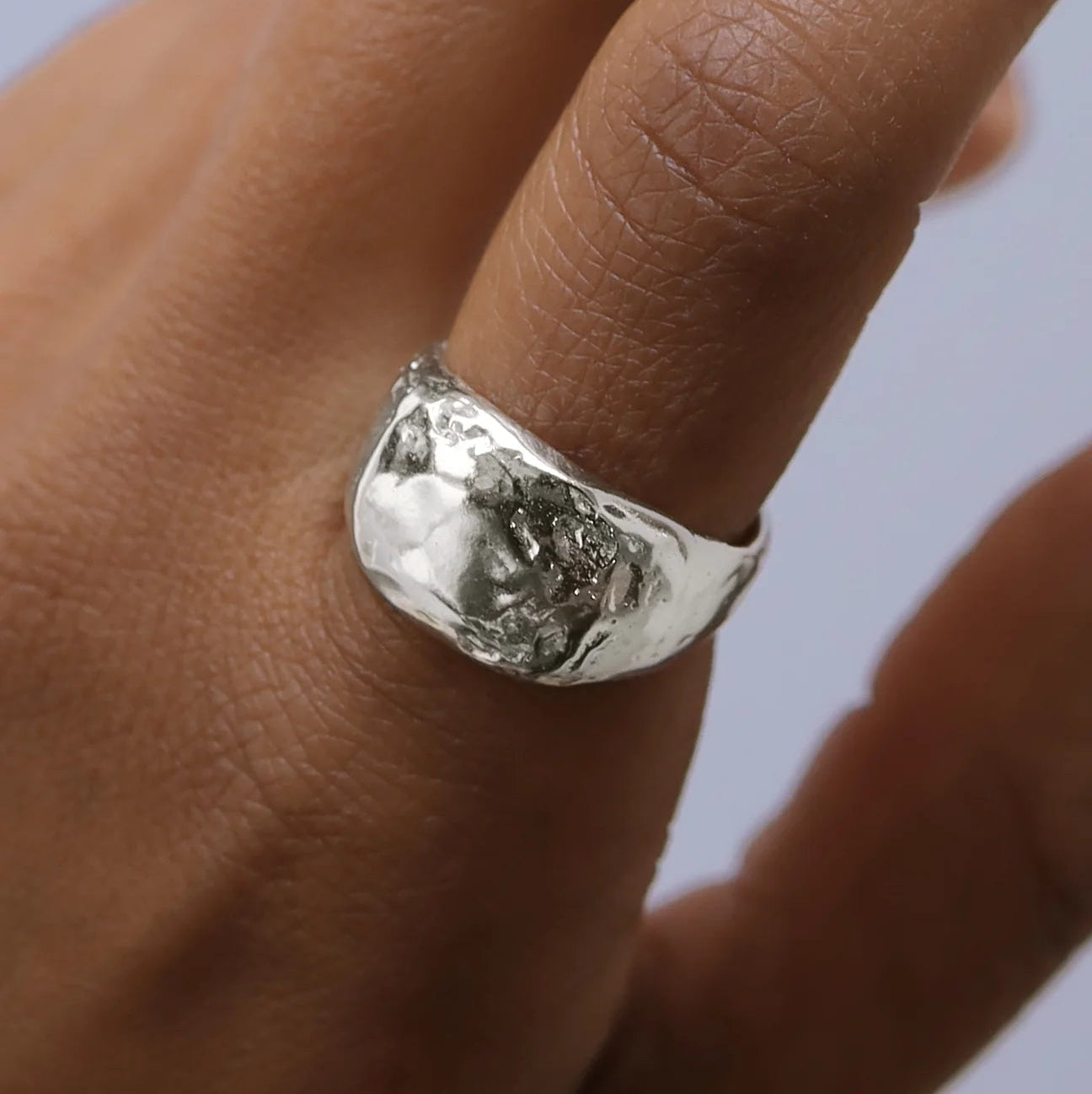 Silver ring on a finger against a neutral background