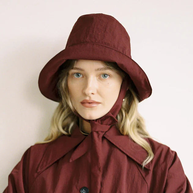 Woman wearing a burgundy coat and hat against a plain background