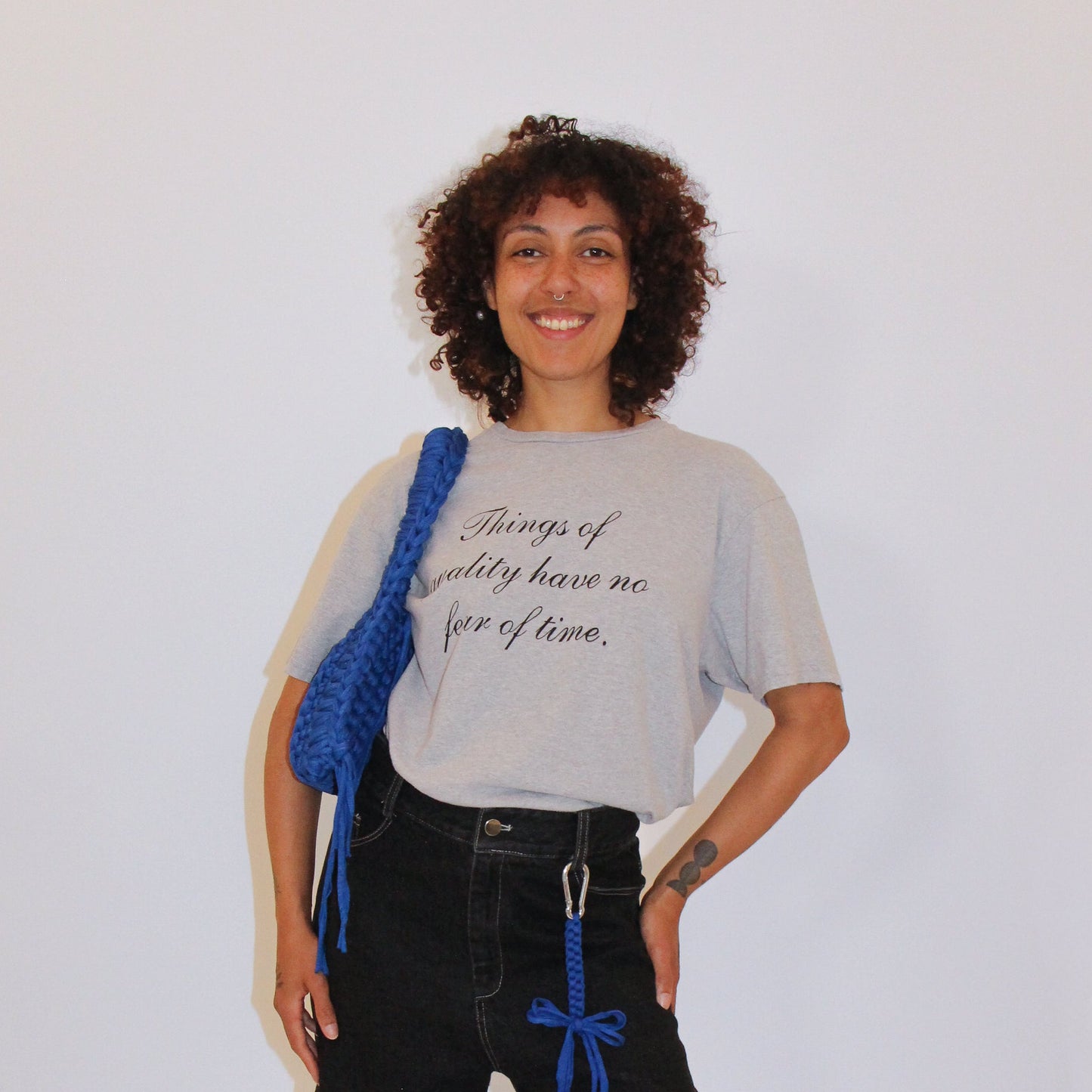 Person wearing a gray t-shirt with text and black shorts with blue ribbons, standing against a white background.