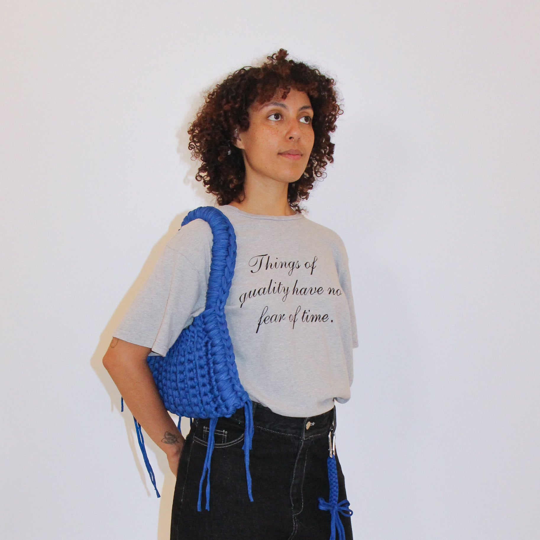 Person wearing a gray t-shirt, black shorts, and carrying a blue knitted bag on a white background