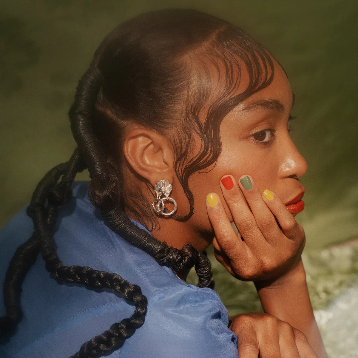 Woman with braided hair wearing a blue top against a blurred natural background