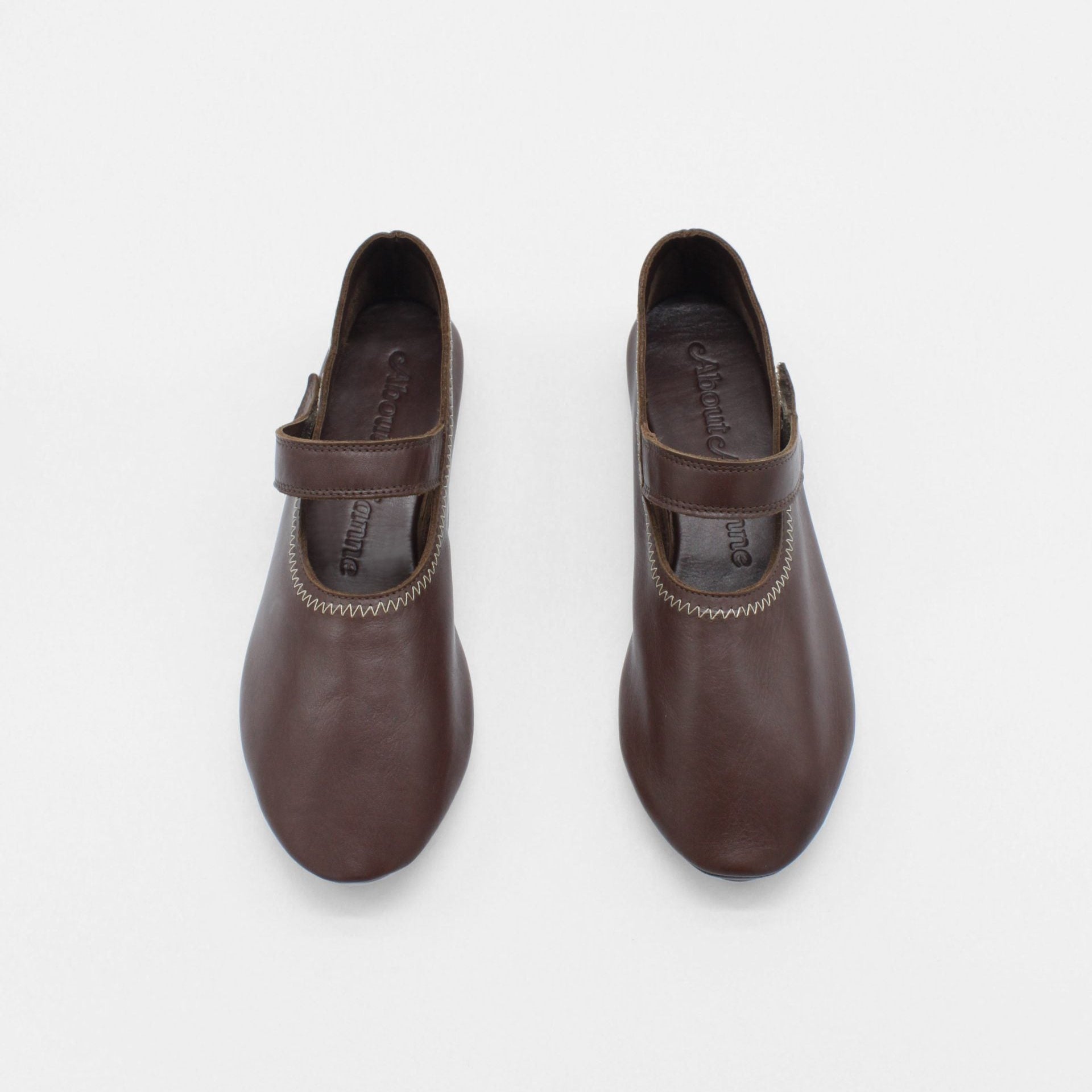 Unlined flat mary-jane made of dark brown lamb nappa leather with a shiny finish and stitching details. 