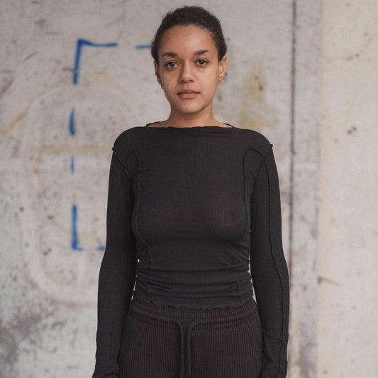 Person wearing a black long-sleeve top and dark pants against a textured wall.