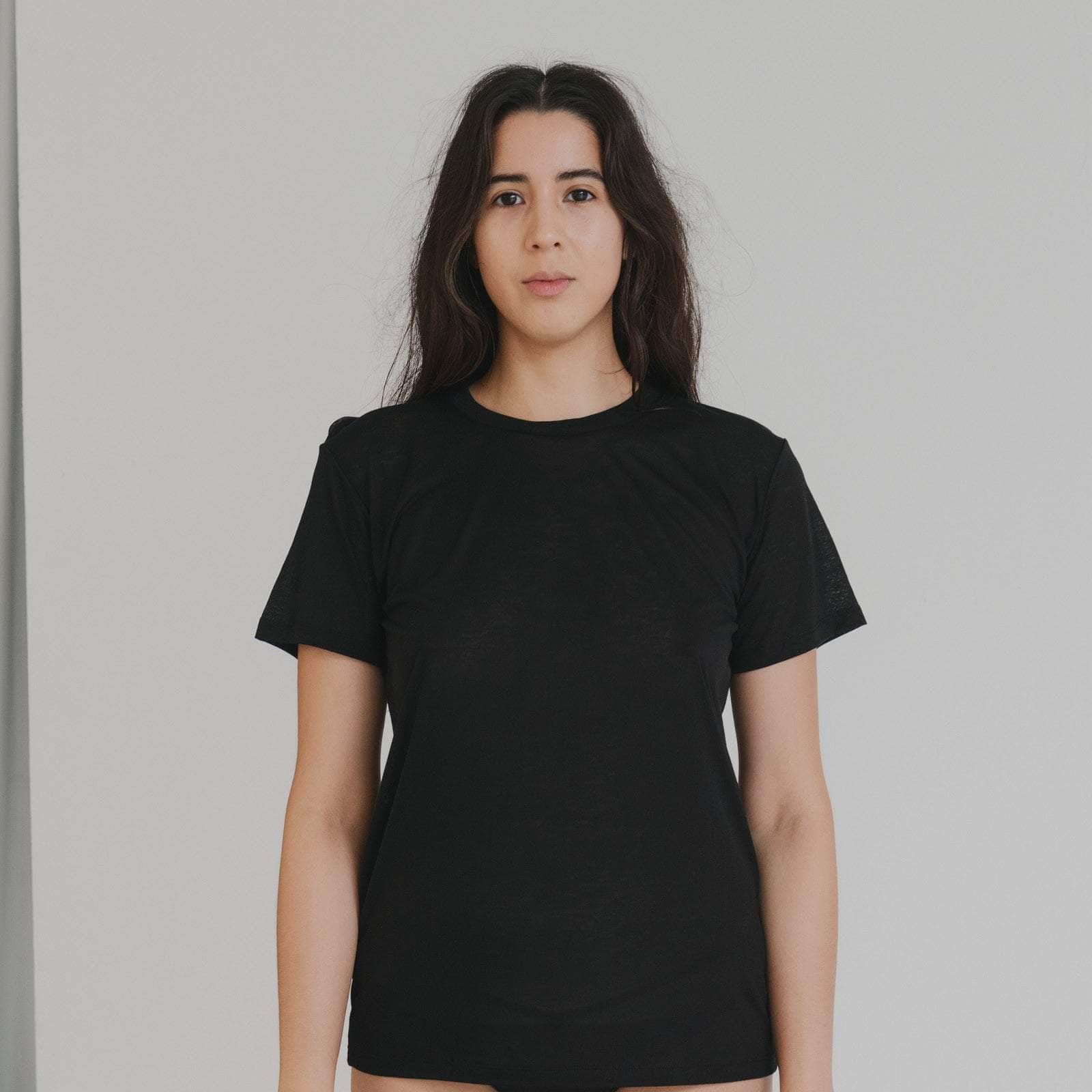 Person wearing a black t-shirt and black underwear against a plain background