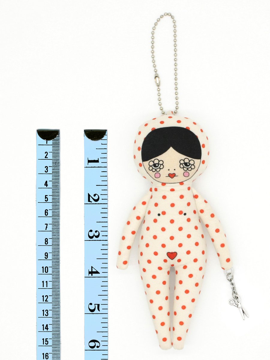 Small doll with polka dot outfit next to a ruler on a white background
