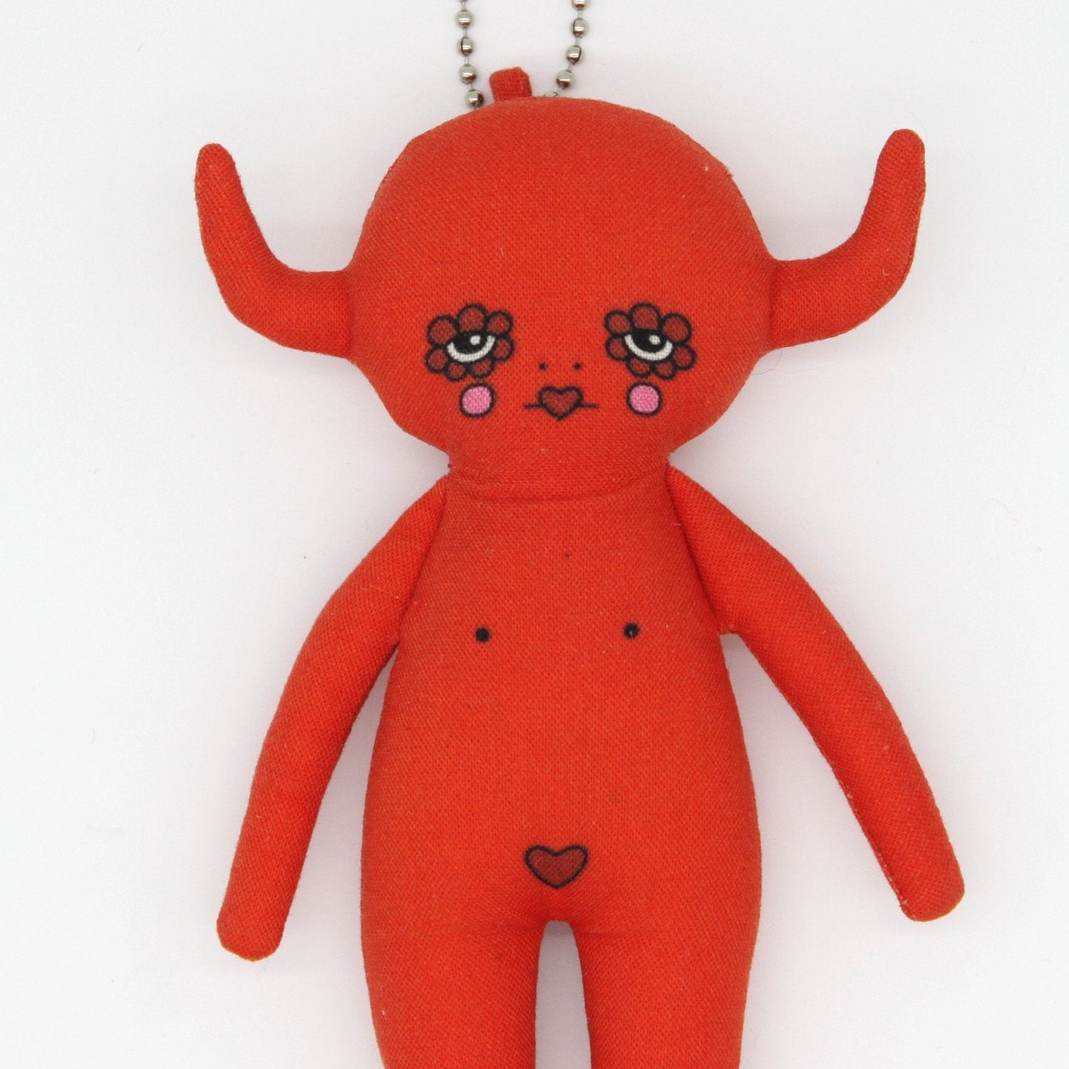 Red plush toy with facial features and a heart on a white background