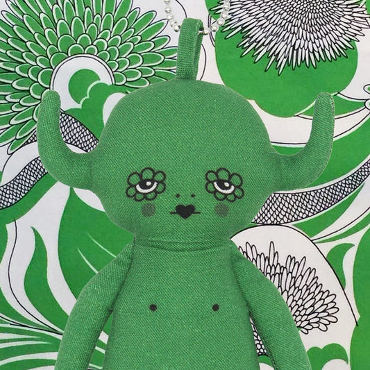 Green plush devil toy charm with floral eyes on a patterned background