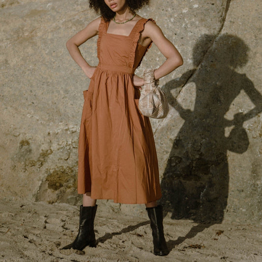 Cinamon coloured apron dress with pockets, defined waist band, large straps at back to tie as bow detail, ruffled shoulder straps, and square neckline