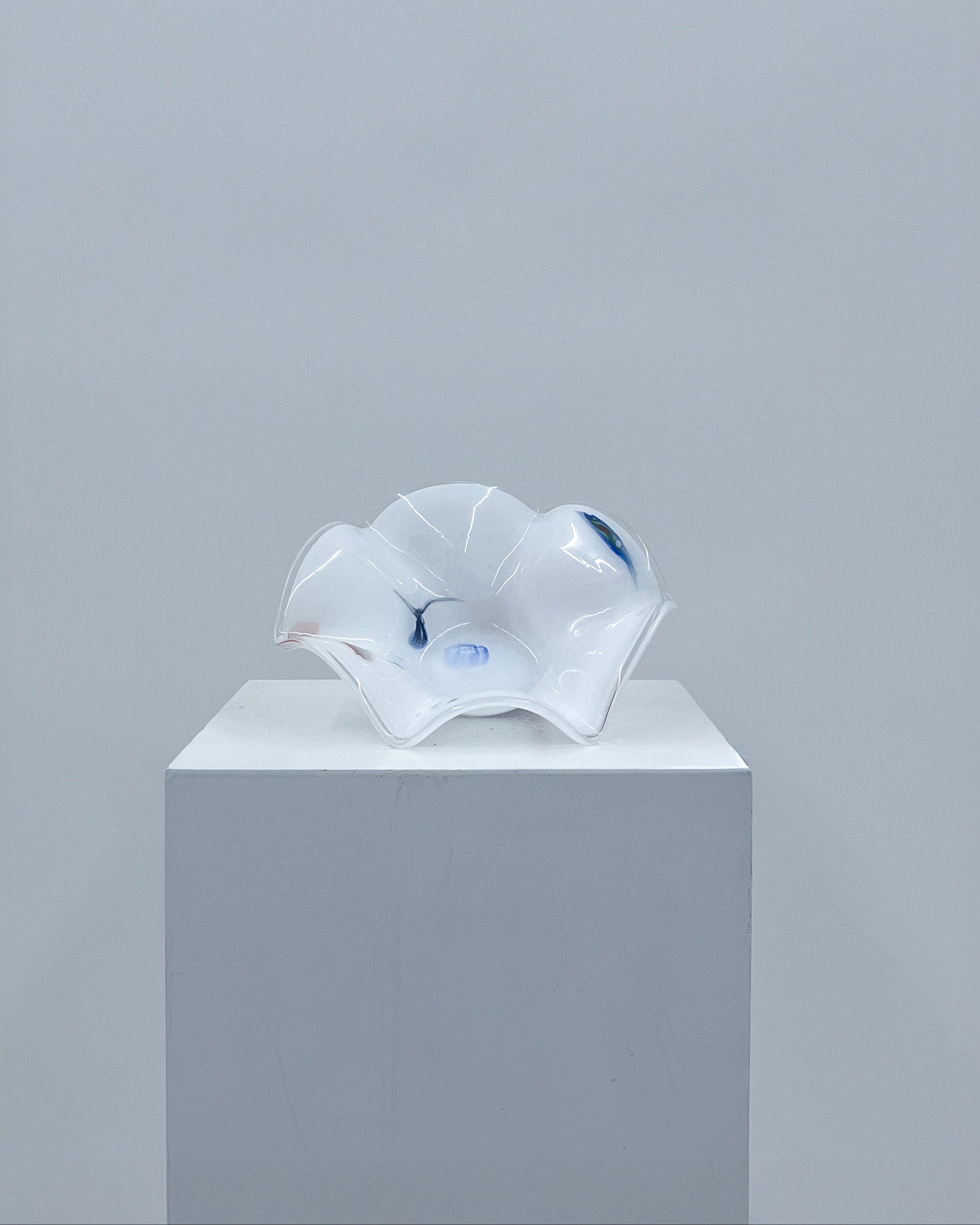 Glass sculpture on a white pedestal against a gray background