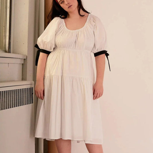 Overall white dress with extra puffy sleeves, gathered tiers, and black bow-tie details, the Jolen dress is both elegant and incredibly comfortable too. It's fully lined with cotton, slips on easily over head, and has pockets. 