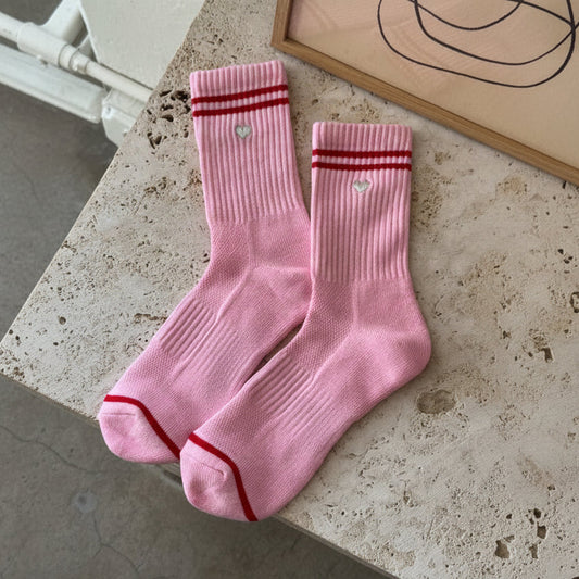 Pink socks with red accents and 'Le Bon Shoppe' branding on a concrete surface.