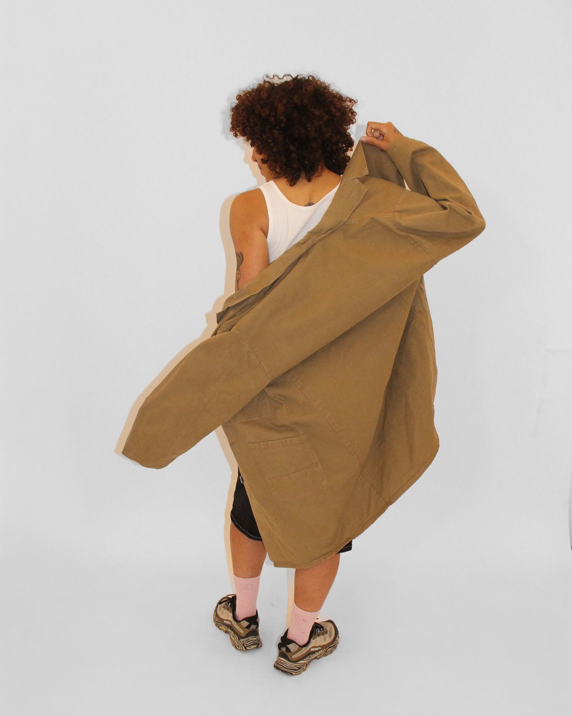 Person wearing a long beige coat over a white top on a light gray background