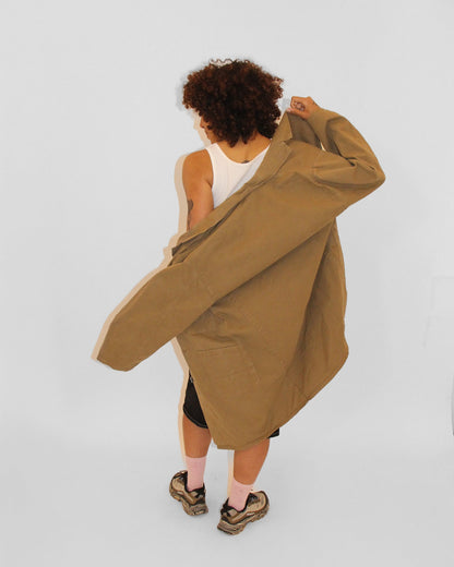 Person wearing a long beige coat over a white top on a light gray background