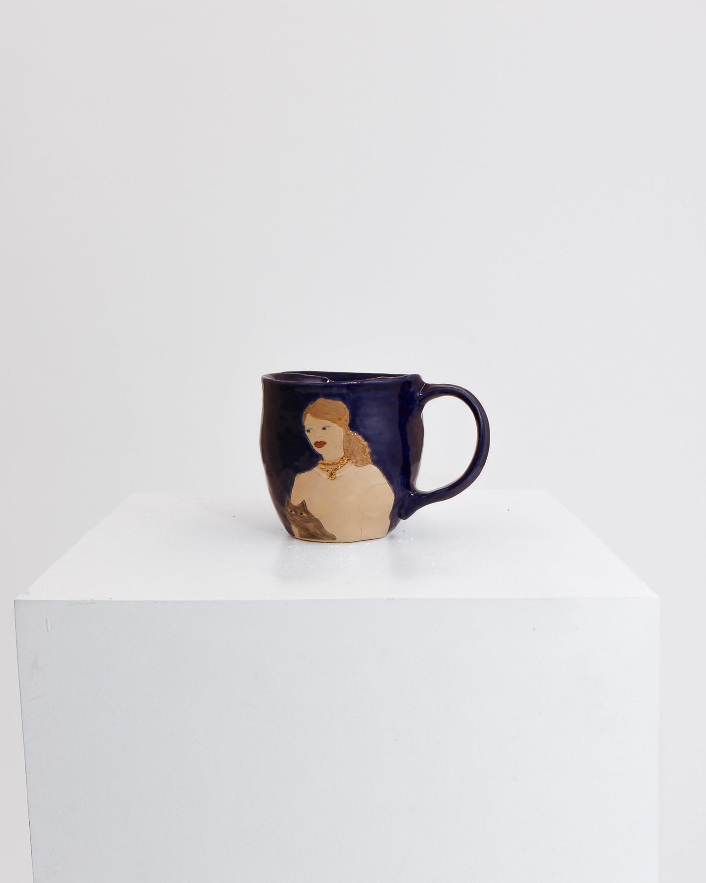 A dark navy blue ceramic mug with a handle, featuring a printed illustration of a woman with blonde hair, displayed on a white pedestal against a white background.