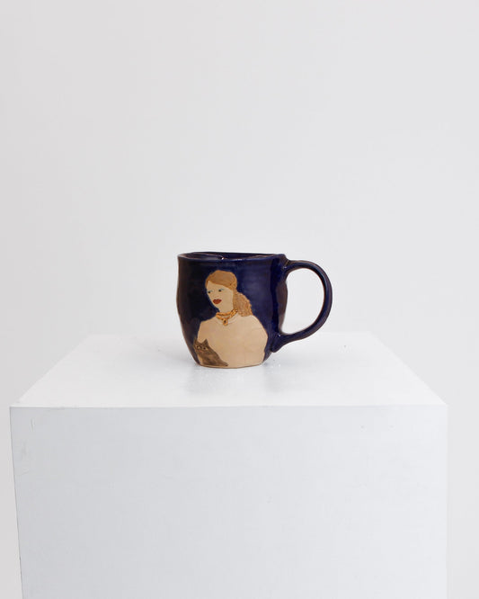 A dark navy blue ceramic mug with a handle, featuring a printed illustration of a woman with blonde hair, displayed on a white pedestal against a white background.