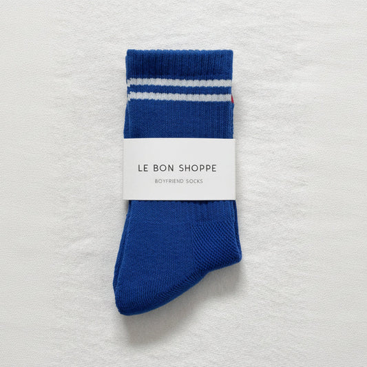 Blue socks with white stripes on a gray textured background, featuring 'Le Bon Shoppe' branding.