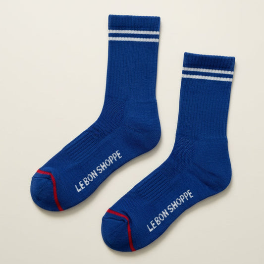 Pair of blue socks with white stripes and 'Le Bon Shoppe' branding on a light gray background