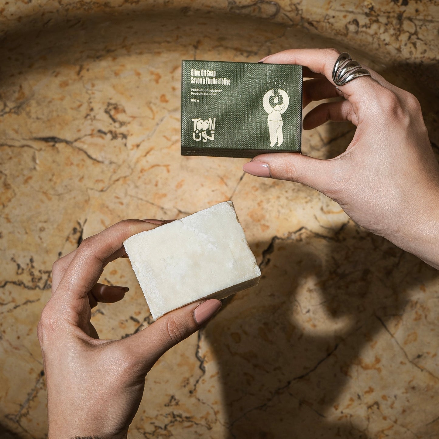 Person holding a bar of soap and its packaging on a textured surface