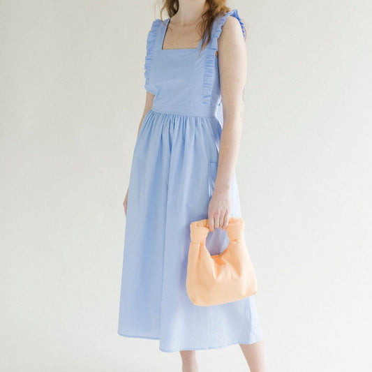 Light blue coloured apron dress with pockets, defined waist band, large straps at back to tie as bow detail, ruffled shoulder straps, and square neckline