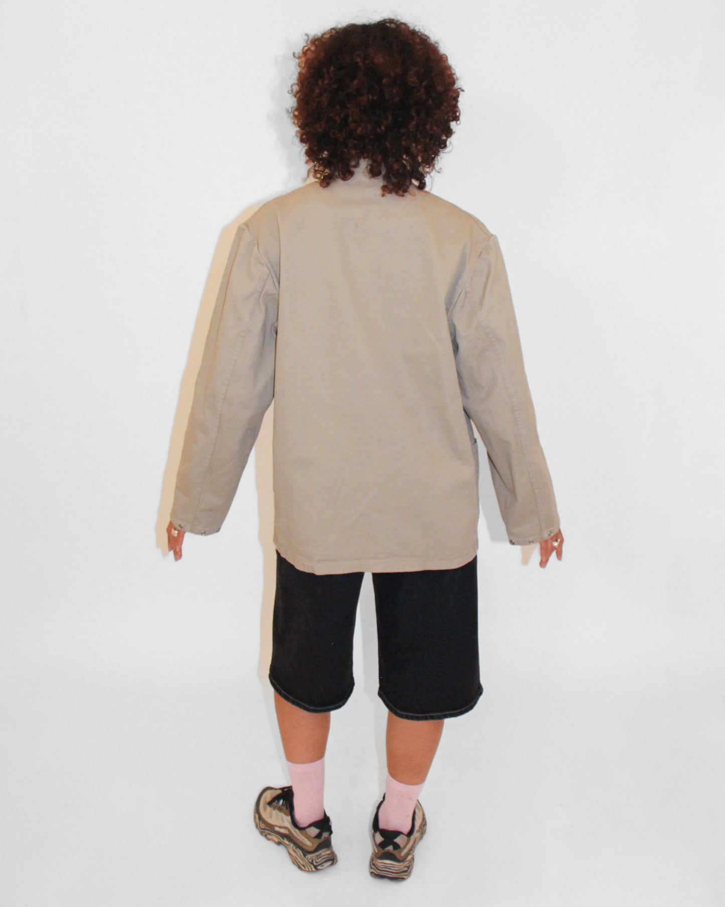 Person wearing a beige jacket and black shorts on a white background
