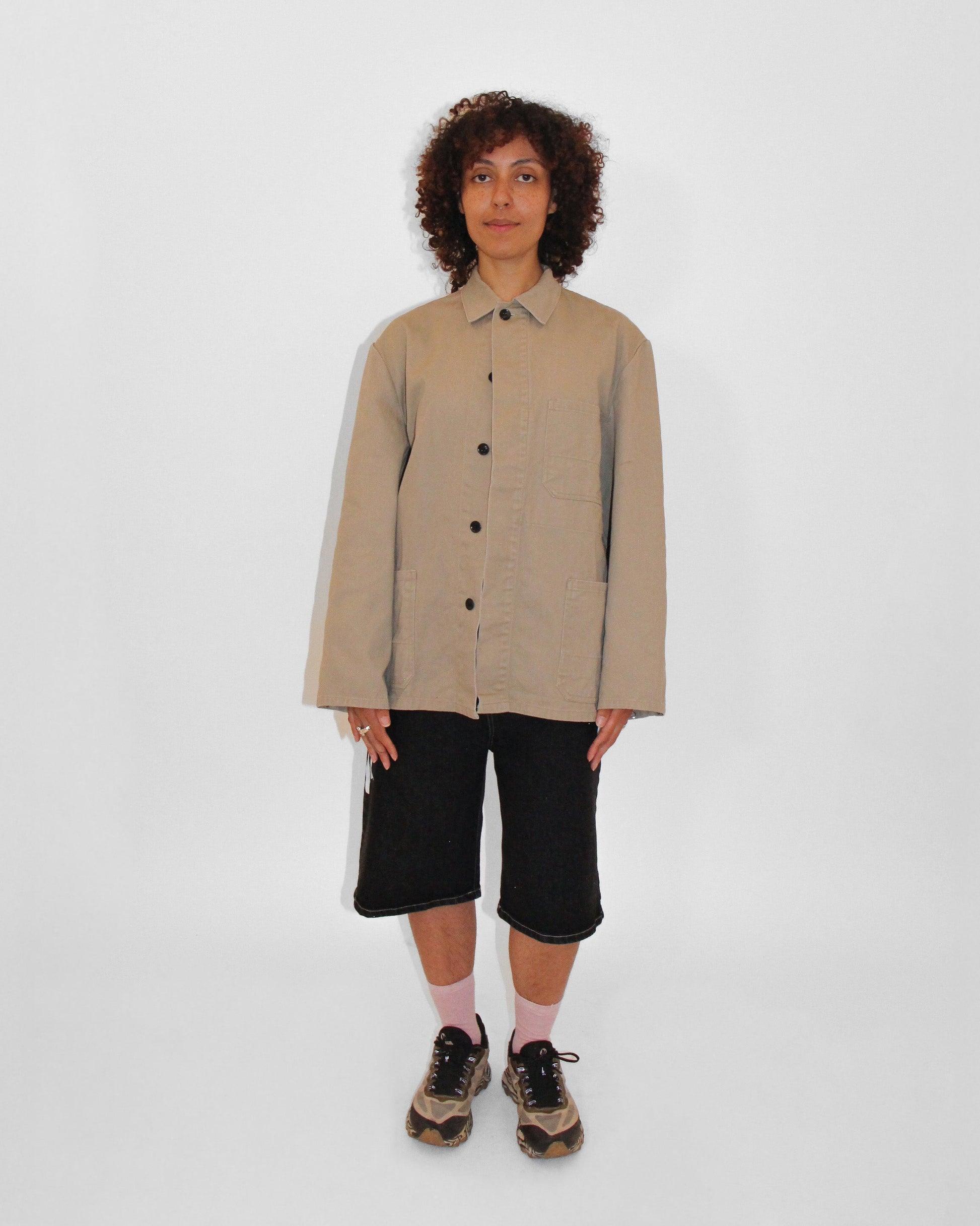 Person wearing a beige jacket with black pants on a white background