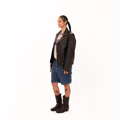 Person wearing a black leather jacket and denim shorts on a white background